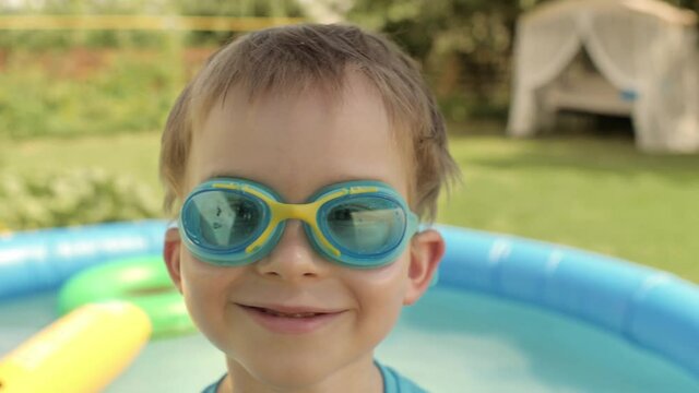 Closeup face of funny baby boy goggles posing at backyard with inflatable rubber swimming pool