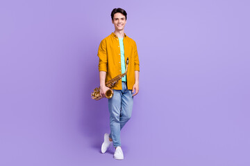 Full length photo of young man happy positive smile hold musical instrument saxophone isolated over...
