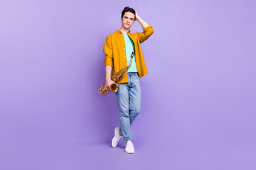 Fototapeta premium Full size photo of nice brunet millennial guy play sax wear brown shirt jeans isolated on violet color background