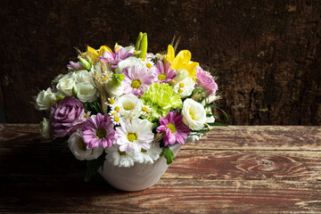 Beautiful bouquet of white, pink and yellow garden flowers in a white vase on a wooden table