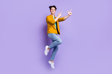 Fototapeta na wymiar Full size photo of cool brunet millennial guy jump point empty space wear shirt jeans isolated on violet color background