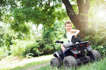 A cute five year old boy rides a black and purple ATV Quad bike in a summer park. © volkonskaya