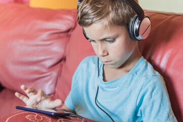 the boy is thinking and listening to music,playing,doing homework online with smartphone.Pupil in headphones.