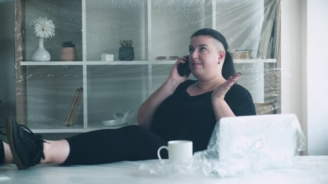 Home office. Distance work. House relocation self-isolation. Pandemic furlough. Worried woman looking for new apartment making phone call in light room covered with plastic wrap.