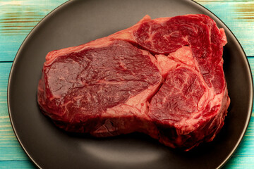 Steak cooking process. The meat is in a black plate. A piece of raw beef on a plate.