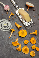 Raw chanterelles, cheese on grater and chopped onion on table.
