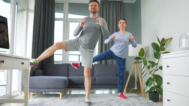 Caucasian couple is doing squats and kicks at home in cozy bright room.