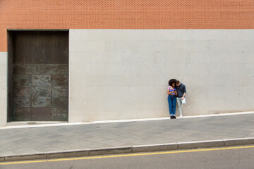 Young white man and black woman using mobile phone in the city with a background wall with copy space