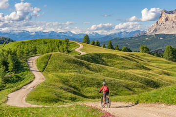 Naklejka premium nice and active senior woman riding her electric mountain bike on the Pralongia Plateau in the Alta Badia Dolomites with awesome Sasso die Santa Cruce summit in Backg, South Tirol and Trentino, Italy