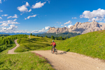 nice and active senior woman riding her electric mountain bike on the Pralongia Plateau in the Alta Badia Dolomites with awesome Sasso die Santa Cruce summit in Backg, South Tirol and Trentino, Italy