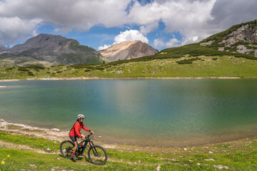Fototapeta premium pretty active senior woman riding her electric mountain bike at Lago de in the Fanes high Valley, part of Fanes-Sennes-Braies nature park in the Alta Badia Dolomites, South Tirol and Trentino, Italy 