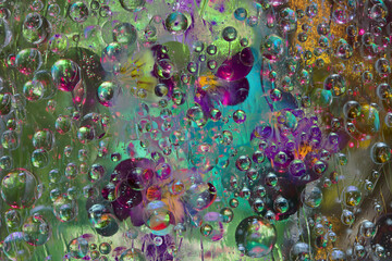 Transparent raindrops falling down against the gold-turquoise-green background with silhouettes of yellow-purple flowers. Abstract fantasy. 3D render.