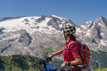 nice and active senior woman riding her electric mountain bike on the Pralongia Plateau in the Alta Badia Dolomites with glacier of Marmolata summit in Background, South Tirol and Trentino, Italy
 - obrazy, fototapety, plakaty