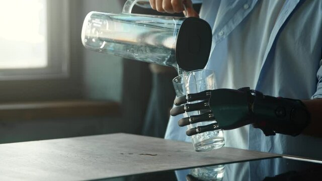 Disabled guy with bio hand prothesis pours water into glass