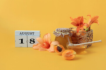 Calendar for August 18 : the name of the month of August in English, cubes with the number 18, honey, a jar of jam, apricots, daylily flowers on a yellow background.