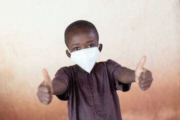 Awesome young black African ethnicity boy wearing a protective face mask showing thumbs up