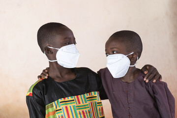 Young siblings from West Africa embracing each other while wearing huge protective masks to prevent...
