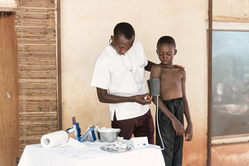 Young black physician measuring blood pressure values in an African boy during routinary health...