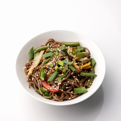 Brown spaghetti or pasta with vegetables and sesame seeds. Bowl isolated on white background. Pan-asian cuisine, spicy food.Top view.