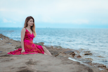 Fototapeta na wymiar Young woman in a pink dress sitting on the beach