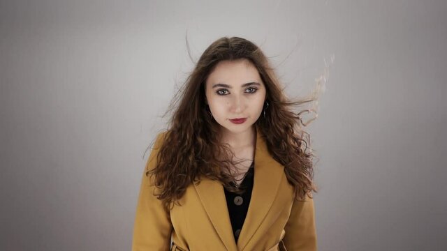 Isolated portrait of woman standing on white background with fluttering hair and flying money in slow motion. Young caucasian lady is posing in front of camera. Theme of professional footage in studio