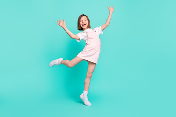 Photo of funky charming school girl wear pink overall smiling dancing isolated teal color background
