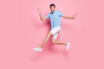 Fototapeta na wymiar Photo of careless athletic man jump run enjoy summer holiday wear blue shirt shorts shoes isolated on pink color background