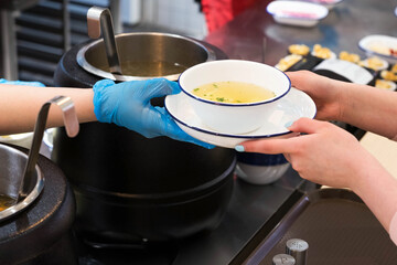 Distribution of food in the dining room. Passing a plate of soup from hand to hand on the background of pots.