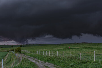 Path in a field of grass on a farm with huge black clouds preparing for a tornado in the sk - Powered by Adobe