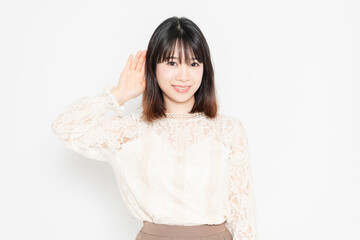 白背景の前に立って、聞き耳を立てる、レースのブラウスを着た若い女性