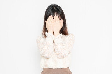 白背景の前に立って、顔を隠す、レースのブラウスを着た若い女性