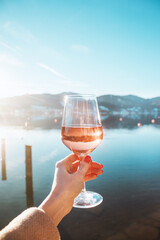Female hand with glass of rose  wine. Cozy pier on the coast of the lake Tegernsee. Alpine...