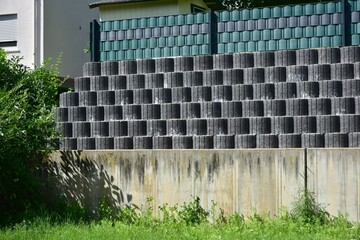 Stützmauer aus grauen runden Pflanzsteinen zur Hangsicherung und Abgrenzung eines Wohngrundstücks gegen die tiefer liegende Straße - obrazy, fototapety, plakaty