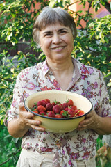 Smiling elderly woman holding a bowl of fresh strawberries in her hands