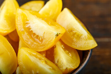 Sliced yellow tomato in a bowl on a wooden background. Vegetable, ingredient and staple food.