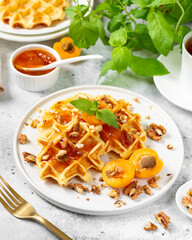 Traditional classic Belgian or Brussels waffles with apricot jam and walnuts in a ceramic plate on a light gray kitchen table closeup