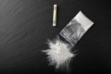 Cocaine in a plastic package on a black background, close-up. A rolled up dollar bill for drug use....