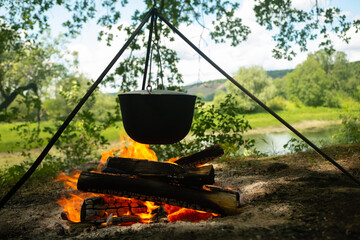 Tourists prepare lunch in hiking pot on campfire at campsite. Bowler on bonfire. Soup boils in cauldron.