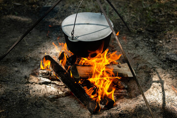 Tourists prepare lunch in hiking pot on campfire at campsite. Bowler on bonfire. Soup boils in cauldron.