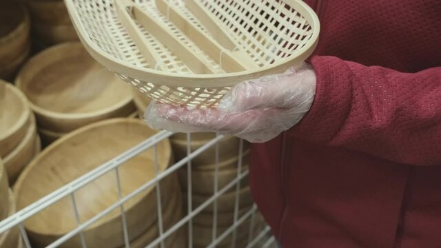 Girl in gloves against virus buys wooden, wicker bread dishes with wooden tongs in a store. Concept of safe shopping and going to malls during epidemics and pandemics of viruses. Hands close up shot