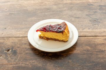 Fluffy portion of cheesecake with strawberry and blueberry jam with biscuit on the base and on a dark table