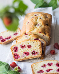 Homemade raspberry loaf cake on parchment paper with fresh raspberries on branches on grey background, selective focus