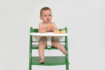 child who is while eating orange  in a highchair on white background