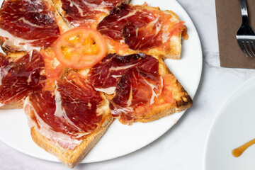 Toasts with delicious Iberian ham and tomato slice, with a fork ready to eat. Typical Spanish dish. Copy space.