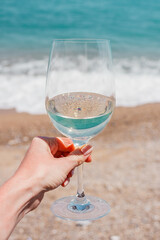 Woman hand with white wine glass on a turquoise Mediterranean sea foam, waves and beach background. Summer vacation in Europe. Nice, French riviera. Alcohol drink photo. 