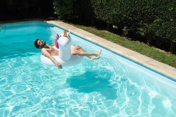 Young man naked on a big unicorn inflatable ring in a swimming pool. Summer concept.