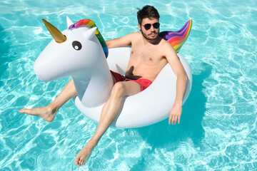 Young man wearing sunglasses on a big unicorn inflatable ring in a swimming pool. Summer concept. © Ladanifer