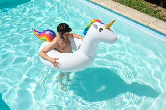 Young man wearing sunglasses inside a big unicorn inflatable ring in a swimming pool. Summer concept.
