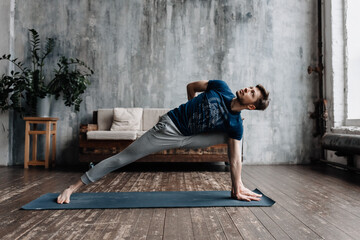 A young man performing yoga asanas and sports exercises to improve the strength and flexibility of...