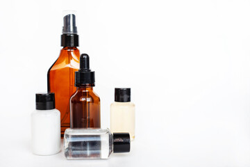 Brown and transparent bottle for liquid cosmetics serum and cream in a jar on a white background. Cosmetologist holding skin care product.